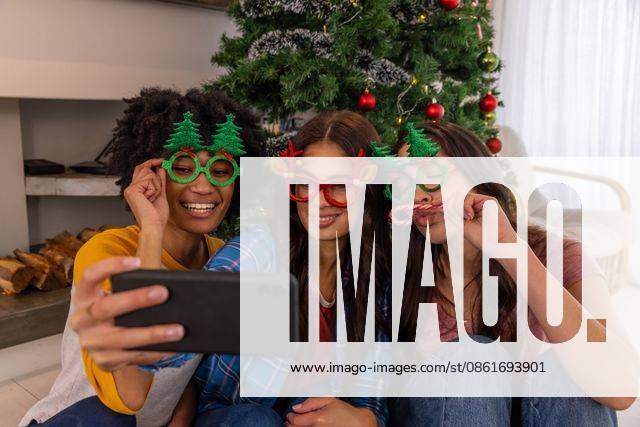 Diverse female friends posing for selfie on living room floor with smartphone near christmas tree, model released, property released, 26.09.2024 06:00:00, 6523222