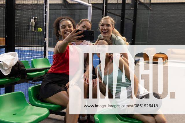 Diverse female friends posing for selfie at padel court in sportswear holding smartphone and racket, model released, property released, 18.06.2025 06:00:00, 6882332