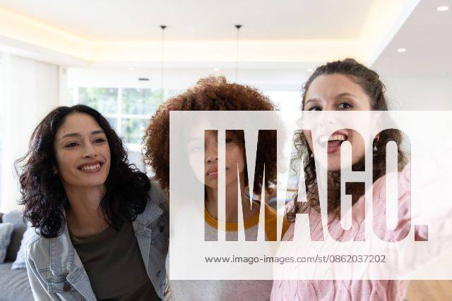 Diverse female friends posing for selfie, smiling, holding smartphone in bright living room sofa, model released, property released, 02.09.2025 06:00:00, 8093909