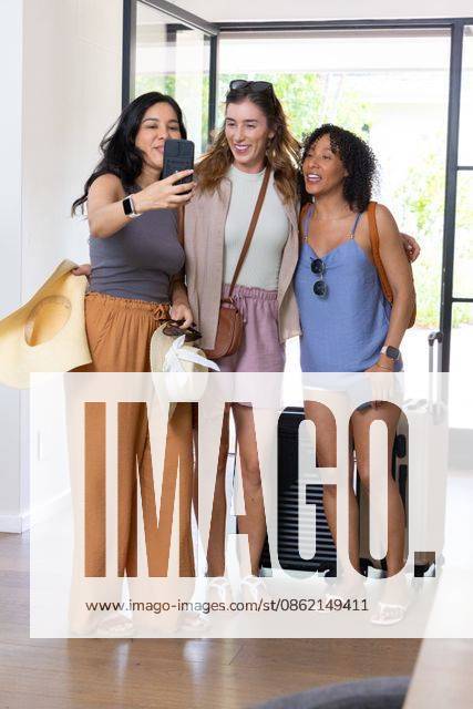 Diverse female friends posing for selfie at entryway holding smartphone, straw hats, suitcase, model released, property released, 11.12.2025 06:00:00, 9757203