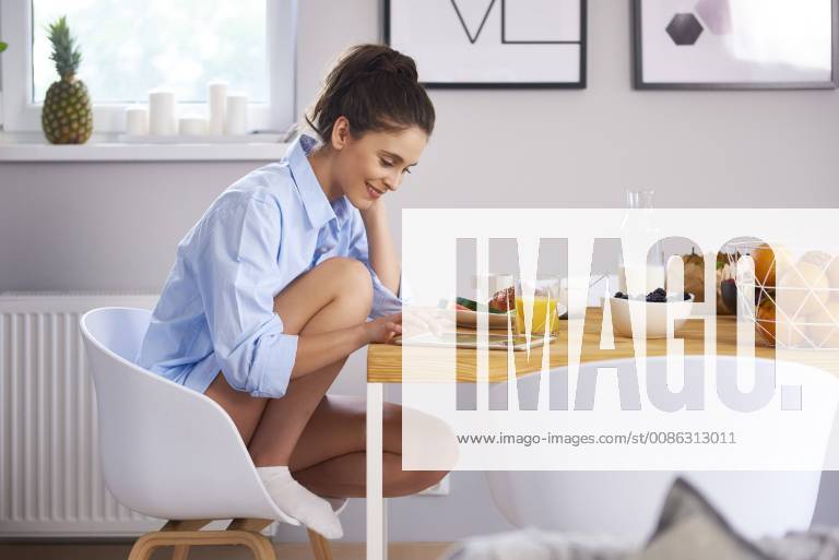 Young woman at home in kitchen, eatinng breakfast, using digital tablet model released Symbolfoto property released ABIF00912