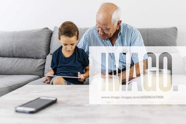 Grandfather and grandson sitting together on the couch at home looking at digital tablet model released Symbolfoto property released JRFF01798