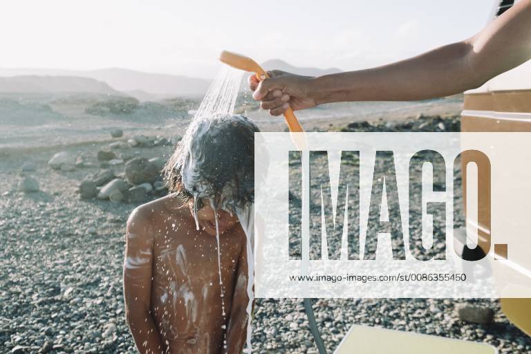 IMAGO Creative: Klimawandel - Nachhaltiges Reisen Boy takes shower outdoors on cobblestone beach, Tenerife, Canary Islands, Spain, Tenerife Canary Islands Spain VISE003988 model released Symbolfoto