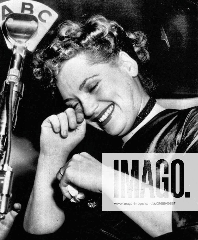 Tearful Winner -- Judy Holliday wipes a tear of happiness from her eye as she stands at microphone in New York night club tonight after hearing announcement that she had won the Oscar for the best 1950 motion picture performance by an actress. She gained the award for her performance as the dumb blonde in Born Yesterday. March 29, 1951. (Photo by AP Wirephoto).
