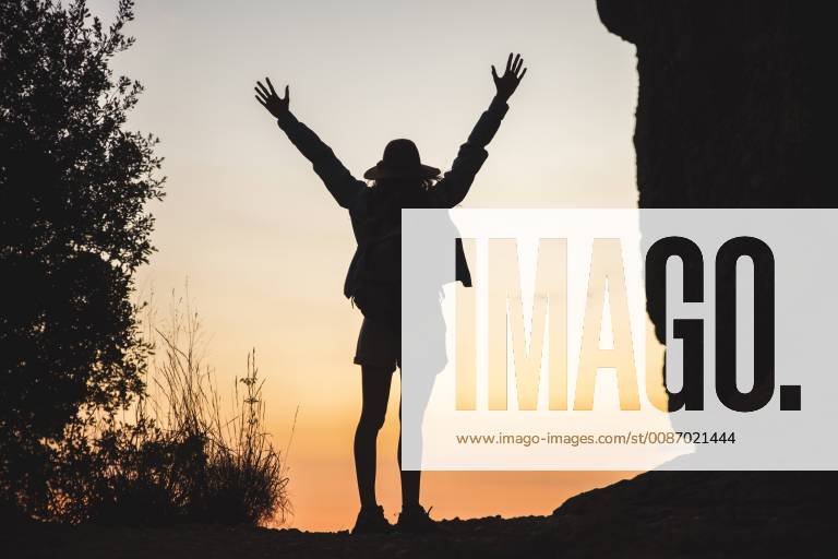 Rear view of woman on a hiking trip raising her arms at sunset model released Symbolfoto AFVF01585