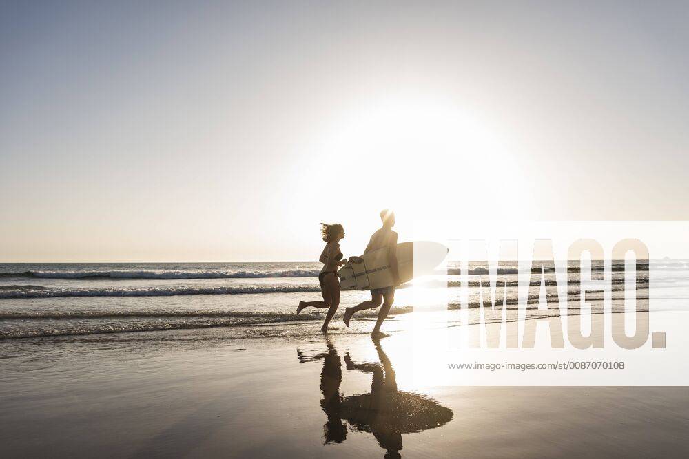 Young couple running on beach, carrying surfboard model released Symbolfoto UUF15120