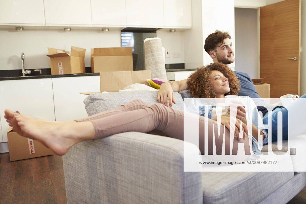 Couple Relaxing On Sofa With Hot Drink In New Home model released Symbolfoto property released