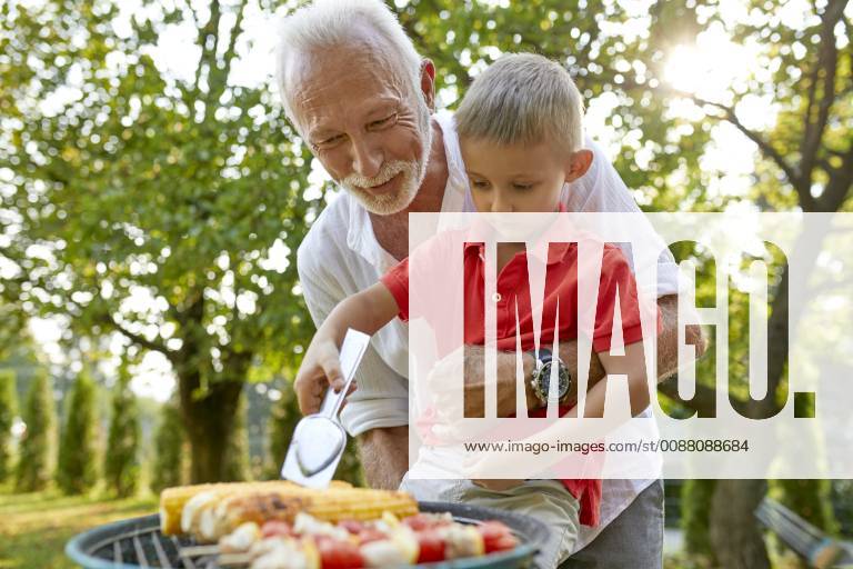 Grandfather helping grandson turning a corn cob during a barbecue in garden model released Symbolfoto property released ZEDF01601