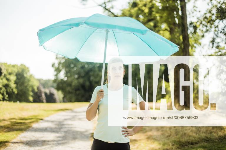 IMAGO Creative, Jahreszeit Sommer, Sonnenschutz Sportive young woman standing in a park holding sunshade model released Symbolfoto MOEF01546