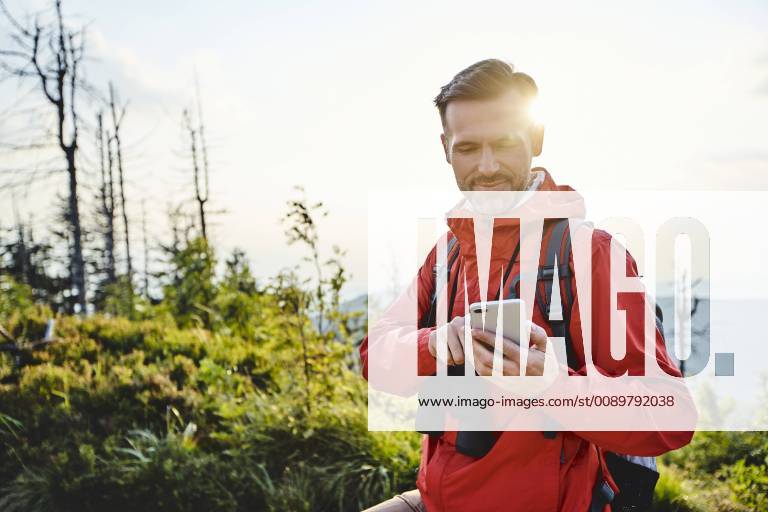 Smiling man checking his cell phone during hiking trip model released Symbolfoto BSZF00740