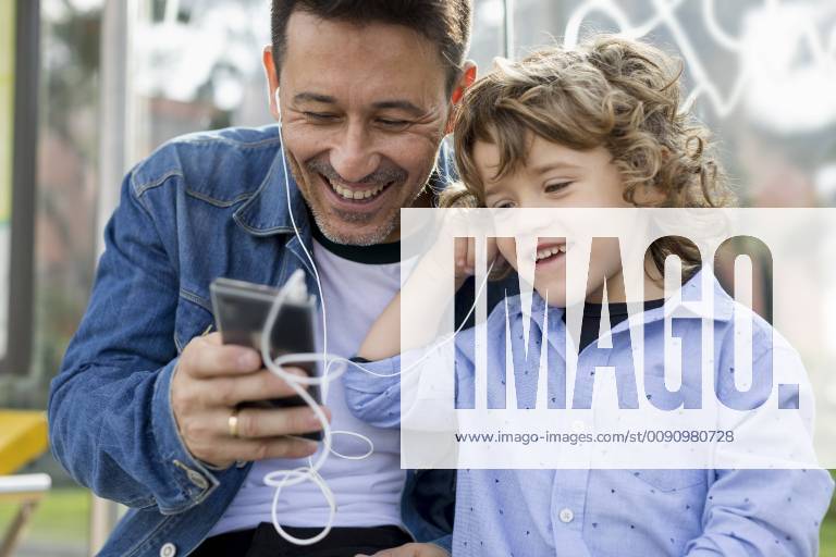 Happy father and son sharing cell phone and earbuds model released Symbolfoto MAUF02274