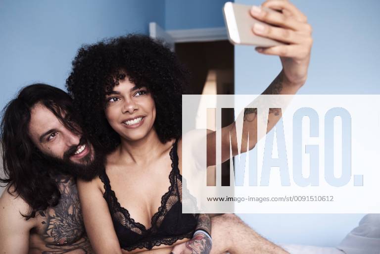 Happy affectionate young couple taking a selfie in bed model released Symbolfoto property released IGGF01070