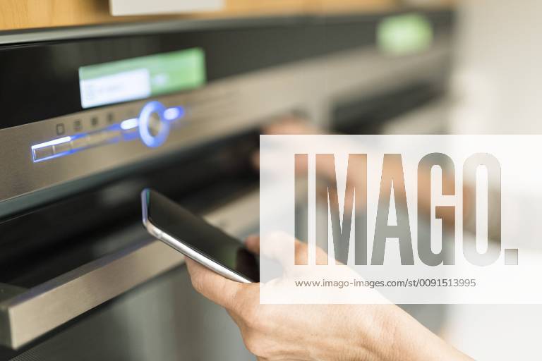 Hand of woman with smartphone checking oven in kitchen at her smart home model released Symbolfoto property released SBOF01888