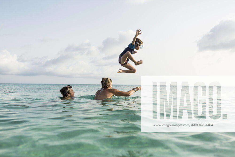 IMAGO Creative, Jahreszeit Sommer, Sommerferien 5 year old son on mother s shoulders leaping into the ocean at sunset 5 year old son on mother s shoulders leaping into the ocean at sunset 58769