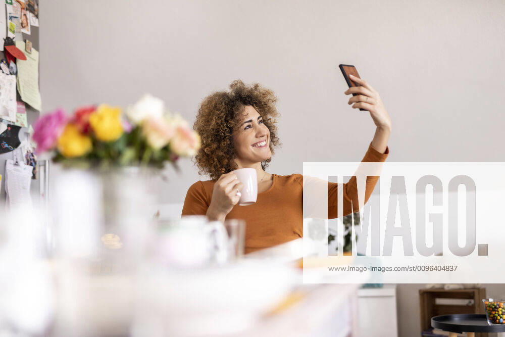 Woman holding coffee cup and taking a selfie at home model released Symbolfoto property released FMKF06072