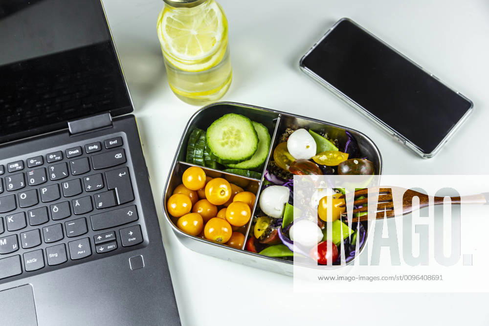 Laptop, smart phone, bottle of lemonade and lunchbox with cucumber slices, winter cherries and quinoa salad (quinoa, cherry tomato, red cabbage, sugar snap peas and mozzarella balls) SARF04410