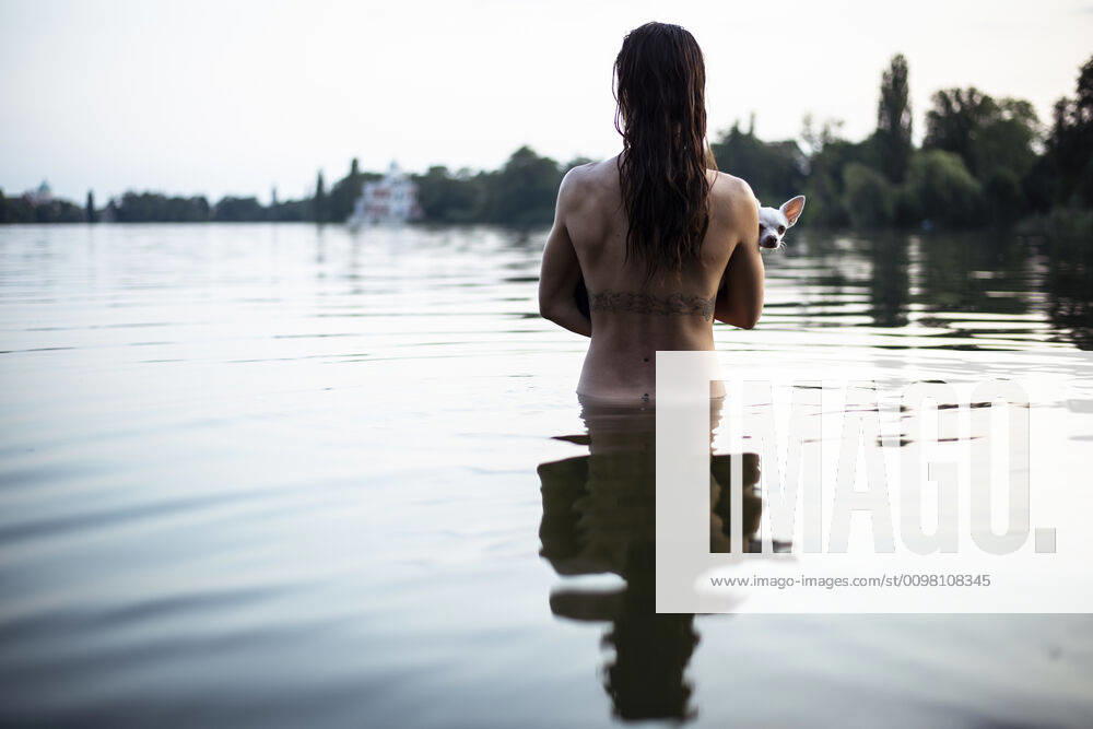 Back view of strong woman holding small dog in natural berlin lake ,model released, Symbolfoto CR_PIDODS200220B-239379-01