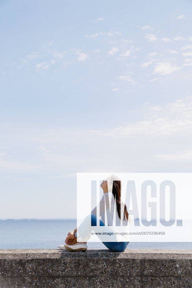 Young Japanese woman sitting on concrete wall by the