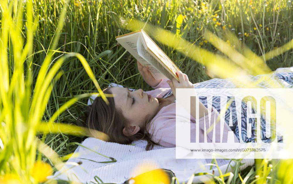 Little girl lying on field of flowers reading a book model released ...