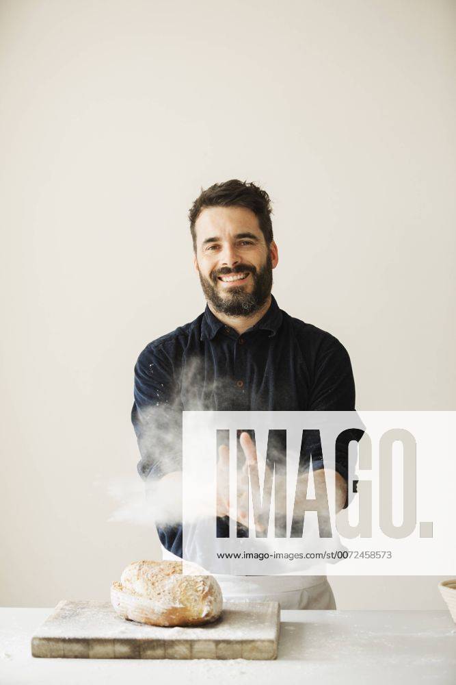 Baker wiping his floury hands, a freshly baked loaf of bread on a