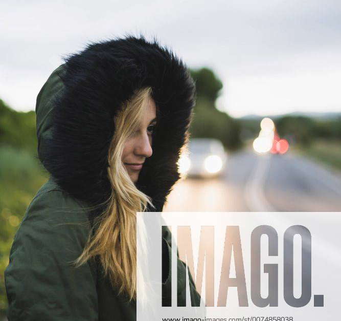 Young woman wearing hooded jacket waiting at roadside in the evening model released Symbolfoto Y