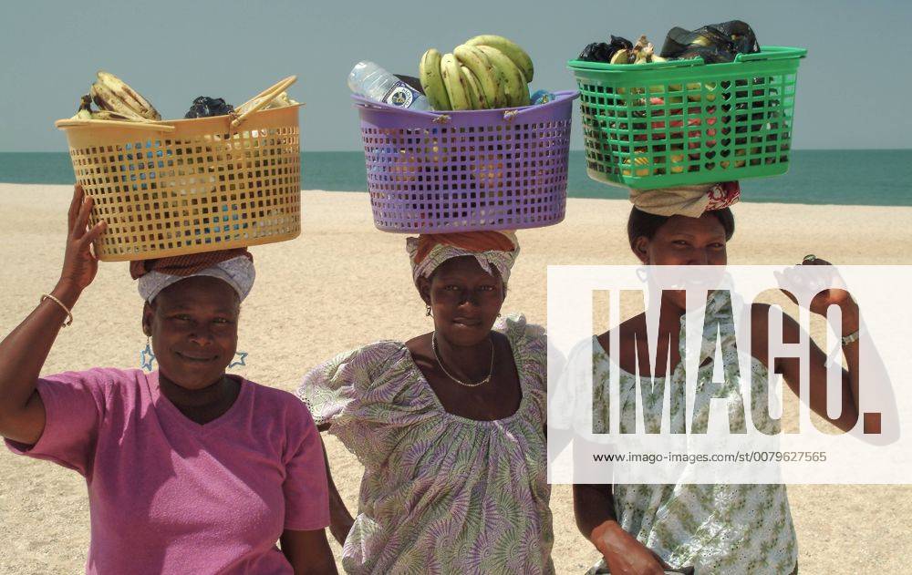 Three smiling local Gambian women selling fruit on a beach in The Gambia