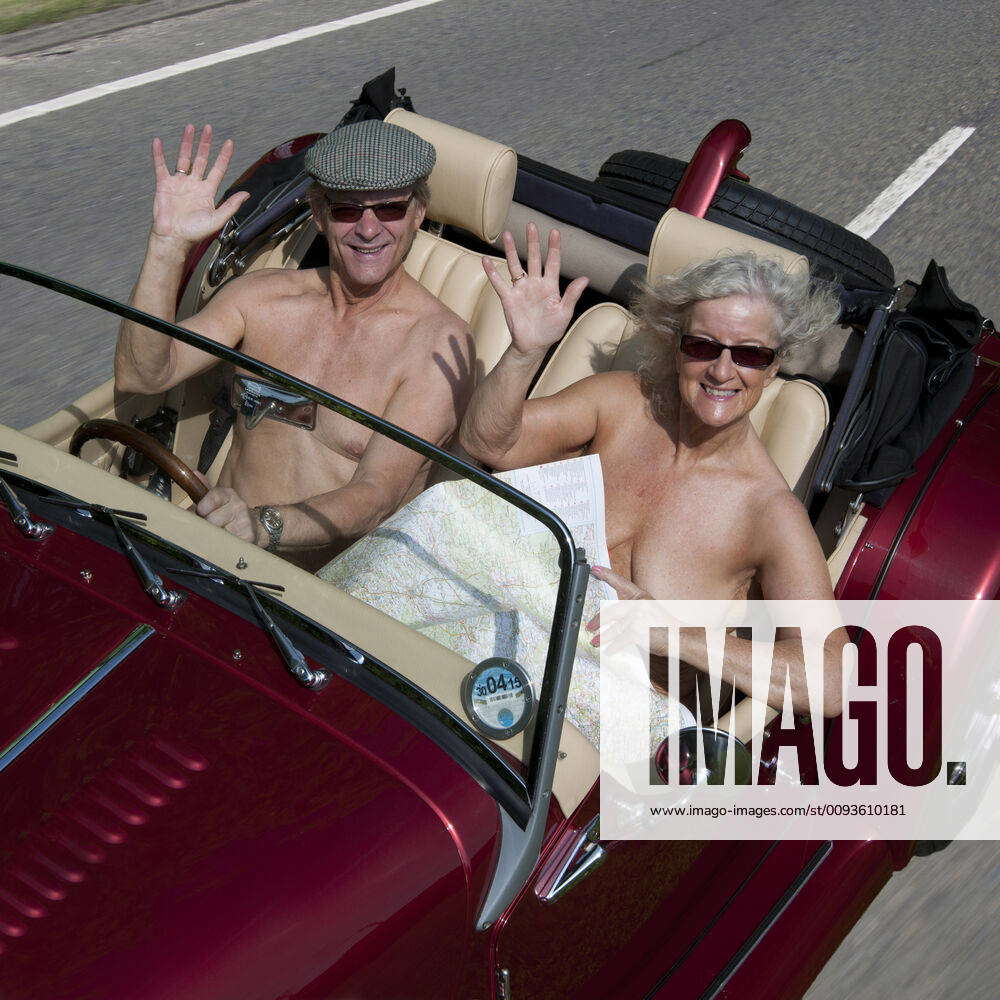 NUDE older couple driving in an open top sports car