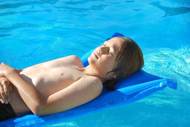 Sunbathing in Pool Teen boy lying wet on an air mattress in the pool on a  sunny day. Y