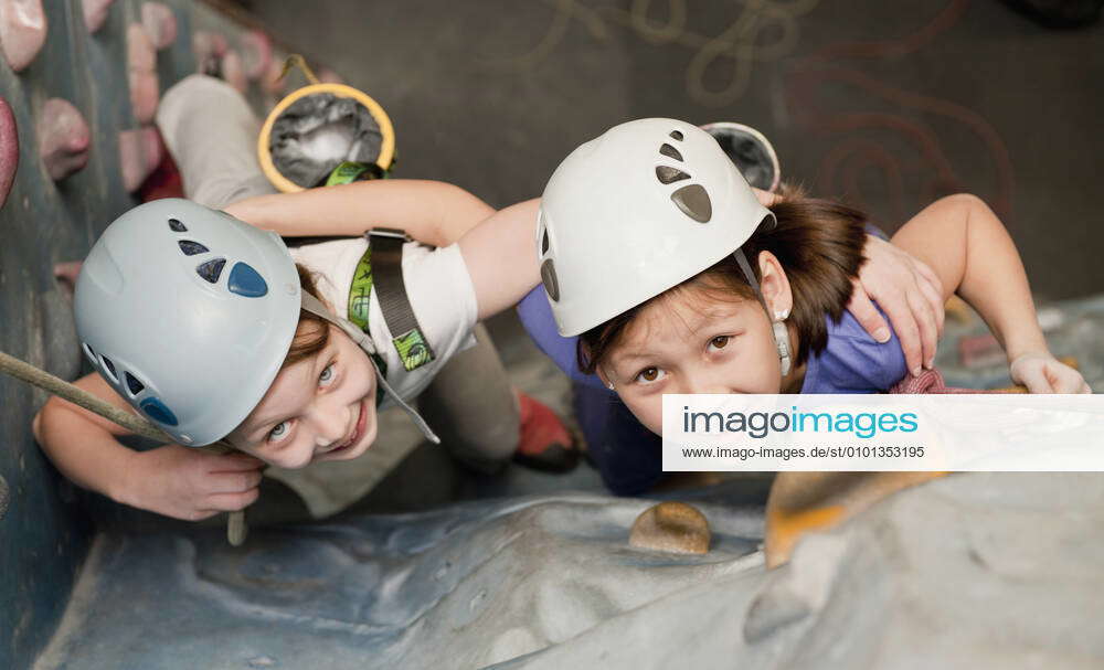 Two young girls climbing at indoor climbing wall in England UK