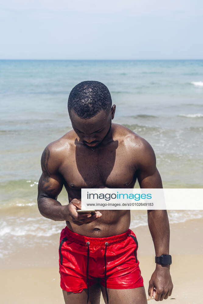 Athletic man using smartphone on beach model released Symbolfoto