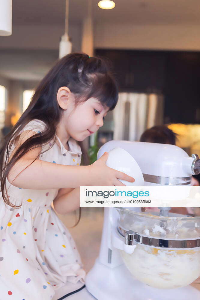 Preschooler baking with her family, adding ingredients to the mixer