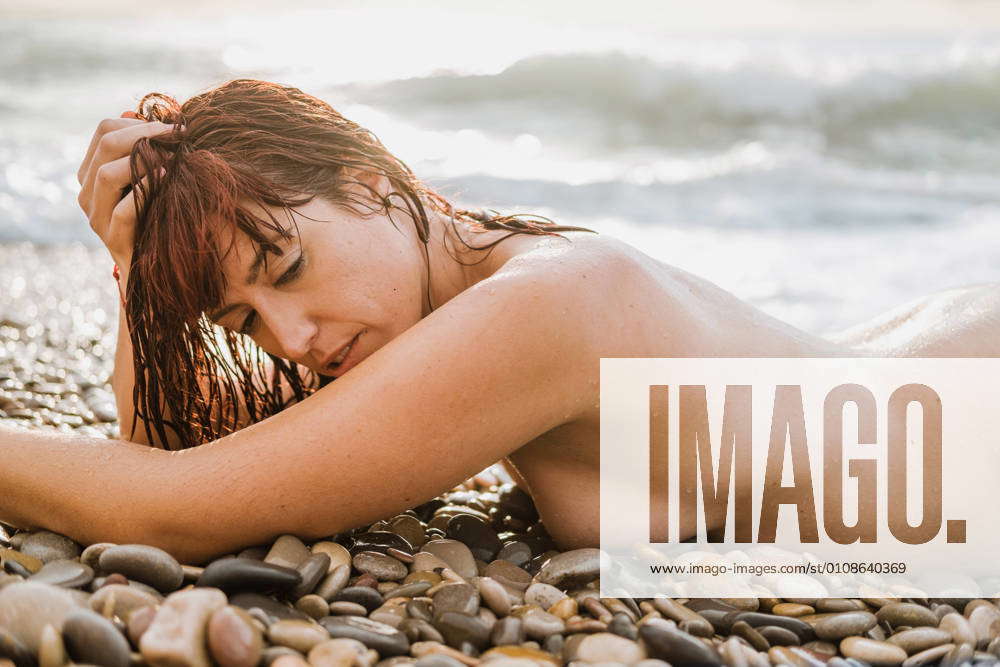 1000px x 667px - Young nude free calm female posing looking away while lying down in a rocky  beach