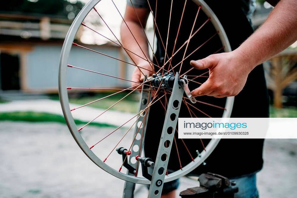 Male person in apron adjusts bike spokes and wheel with service tools