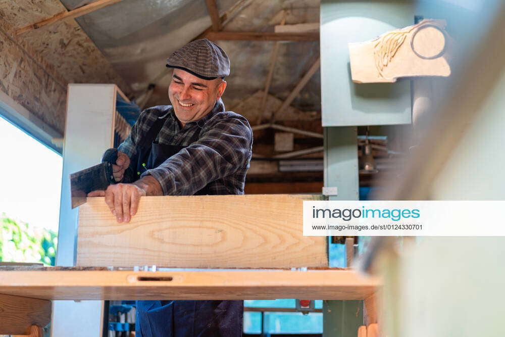 Happy carpenter using sharp saw while cutting lumber plank at workbench ...