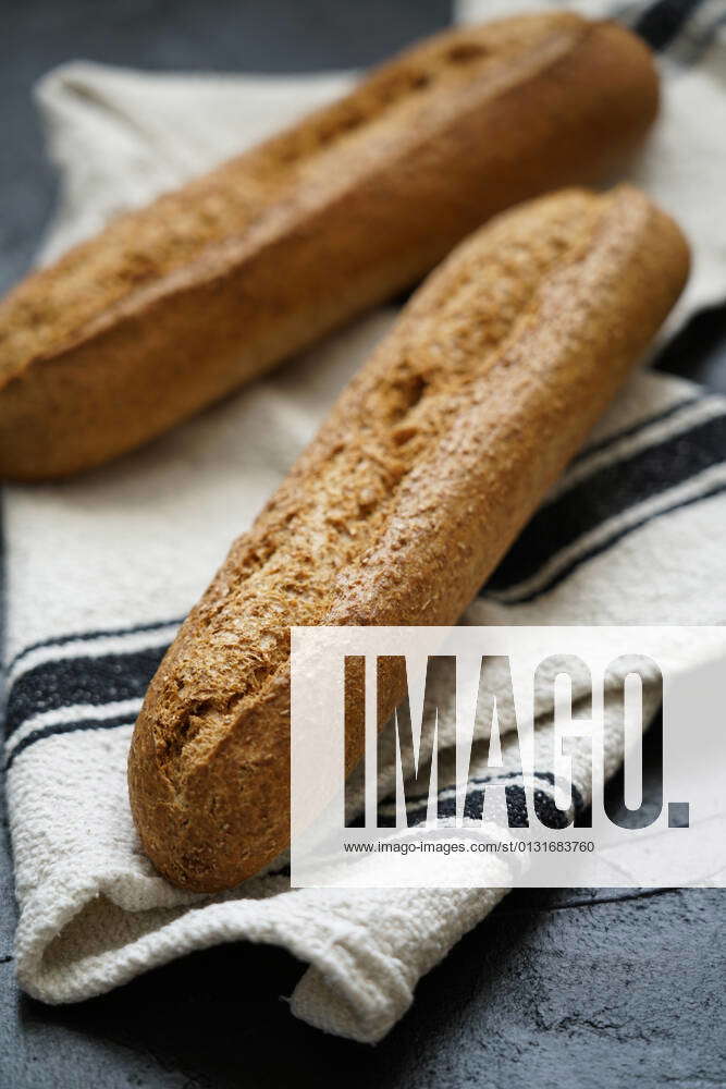 Loaf of fresh baked artisan whole grain baguette bread on raw linen ...