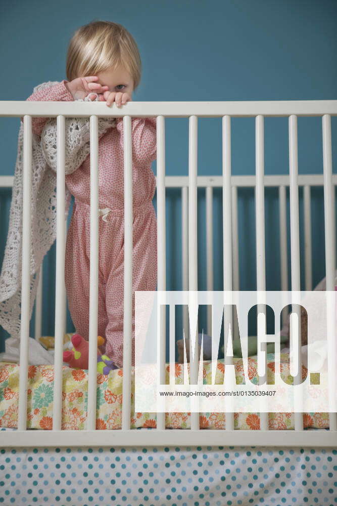 Portrait of female toddler hiding behind comfort blanket in crib