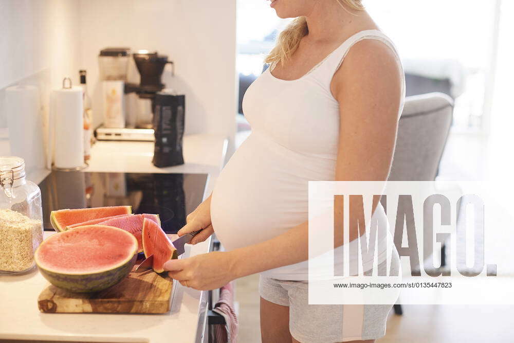 Cropped shot of pregnant young woman slicing melon in kitchen
