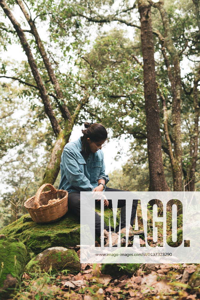 Happy smiling female mycologist sitting on mossy boulder with basket ...