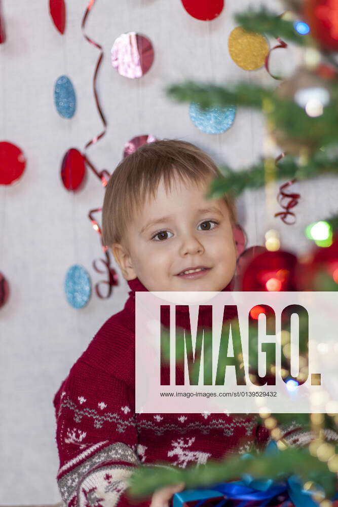 A child at the Christmas tree with garlands puts gifts under it