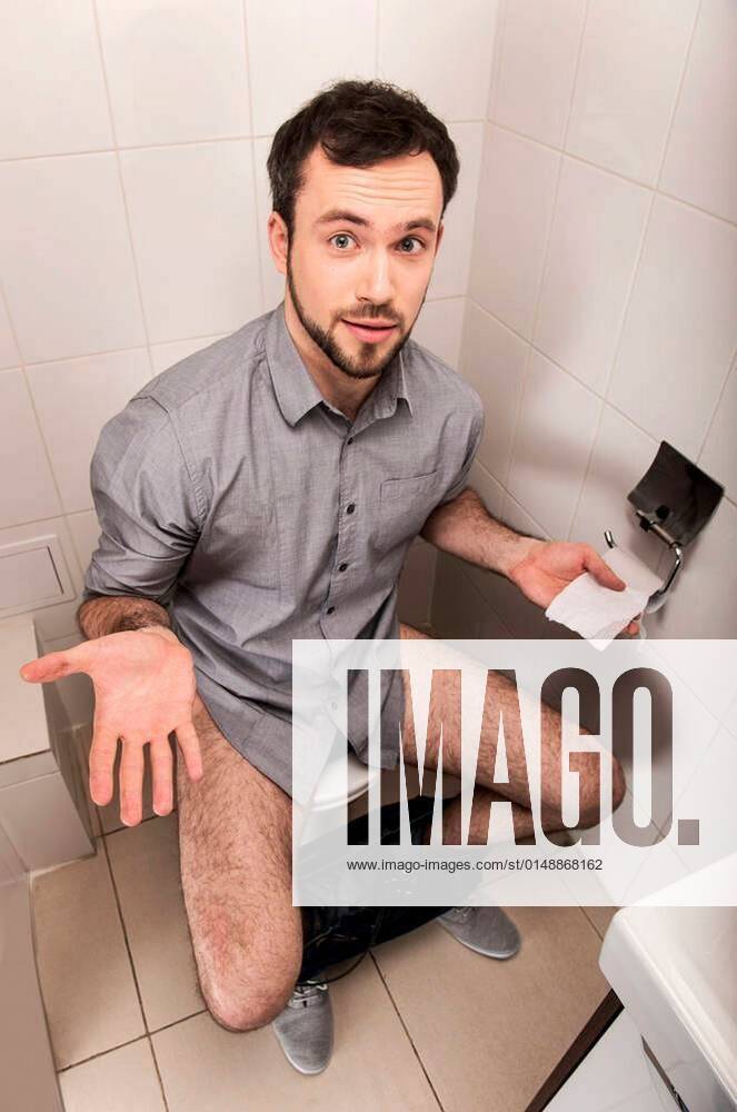 Close-up of man in toilet holding tissue. Adult man sitting on bathroom ...