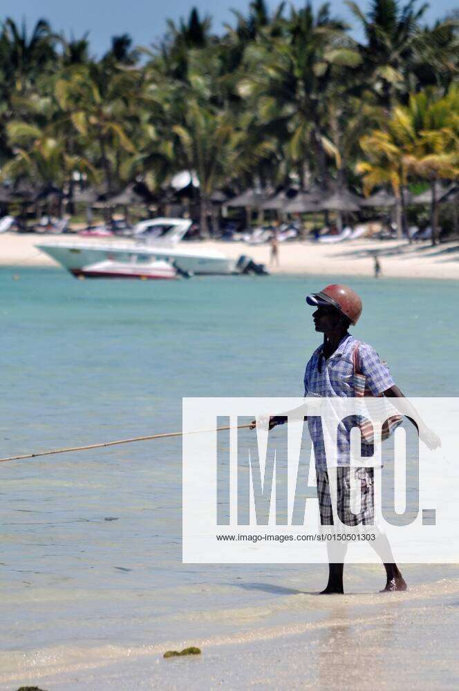 Mauritius, a man fishing wearing a motorbike helmet as hat at Belle Mare  beach xagefotostockx