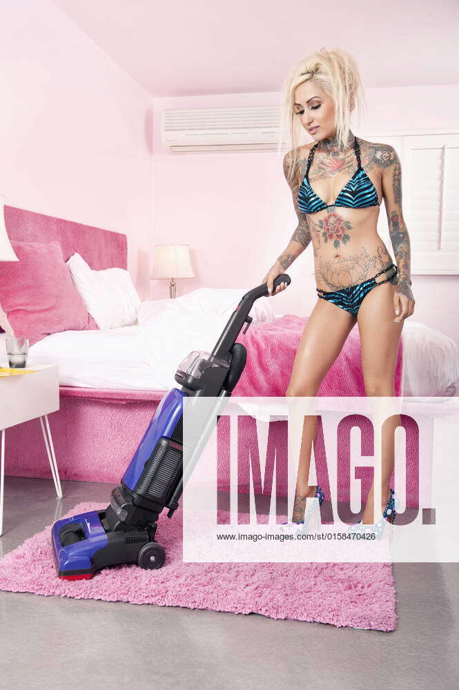 Sexy young tattooed woman in bikini vacuuming bedroom model