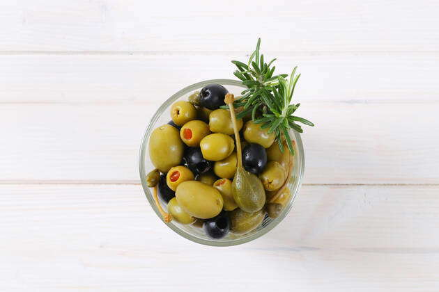 Glass of pickled olives, capers and caper berries on white wooden ...
