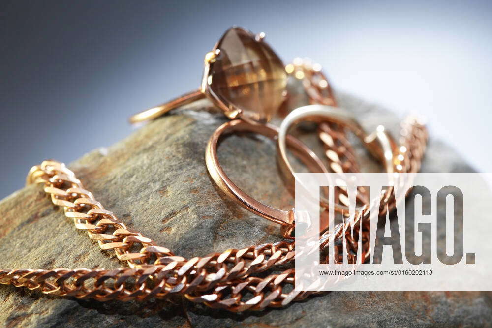 Gold rings and chain on gray stone against nice dark background