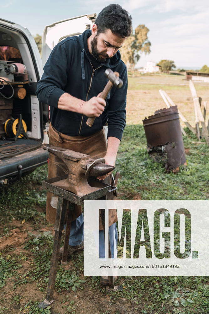 Worker in uniform horseshoe with hammer on metal anvil while