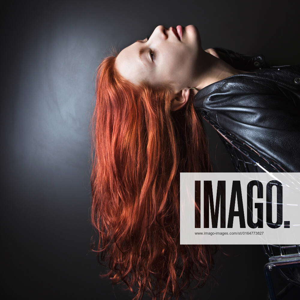 Pretty redhead young woman wearing leather jacket leaning back in chair  with long hair hanging