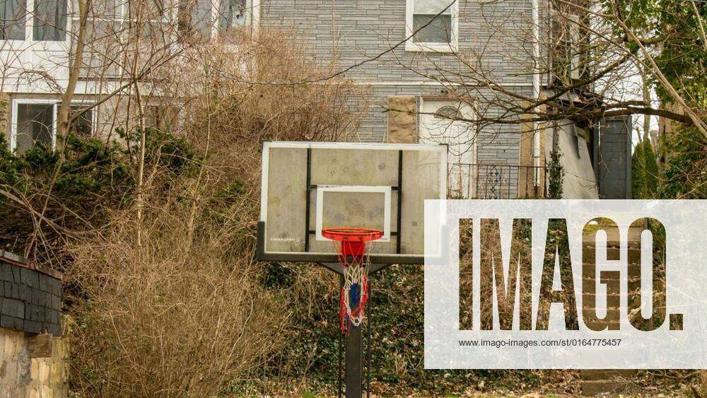 A Basketball Net Hanging in Front of An Overgrown Home, A Basketball
