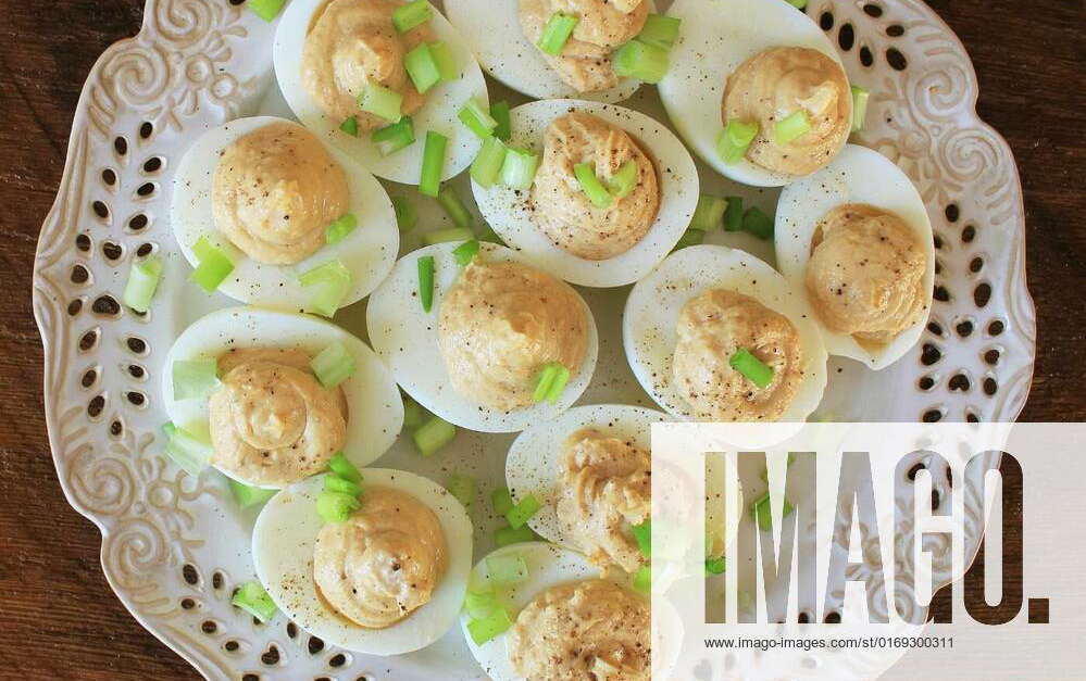 Deviled eggs with cod livers with leek on white plate. Rustic wooden