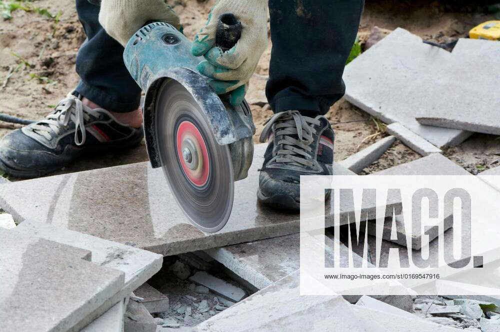 A worker with a circular saw cuts a tile in closeup., A worker with a