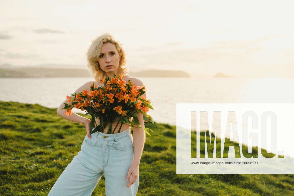 Topless female with breast covered with bunch of fresh orange flowers
